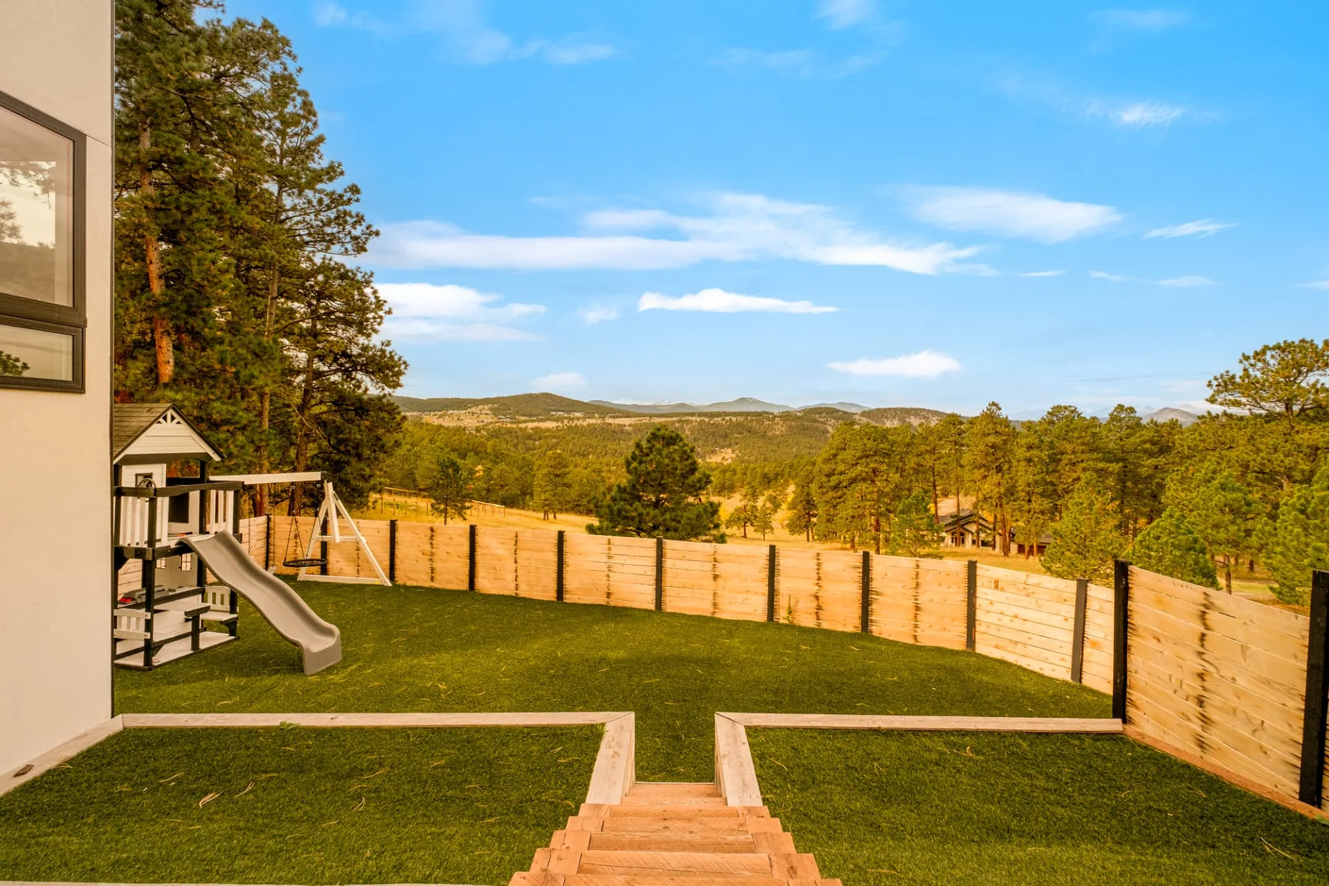 Terraced turf back yard with a play set and fenced perimeter