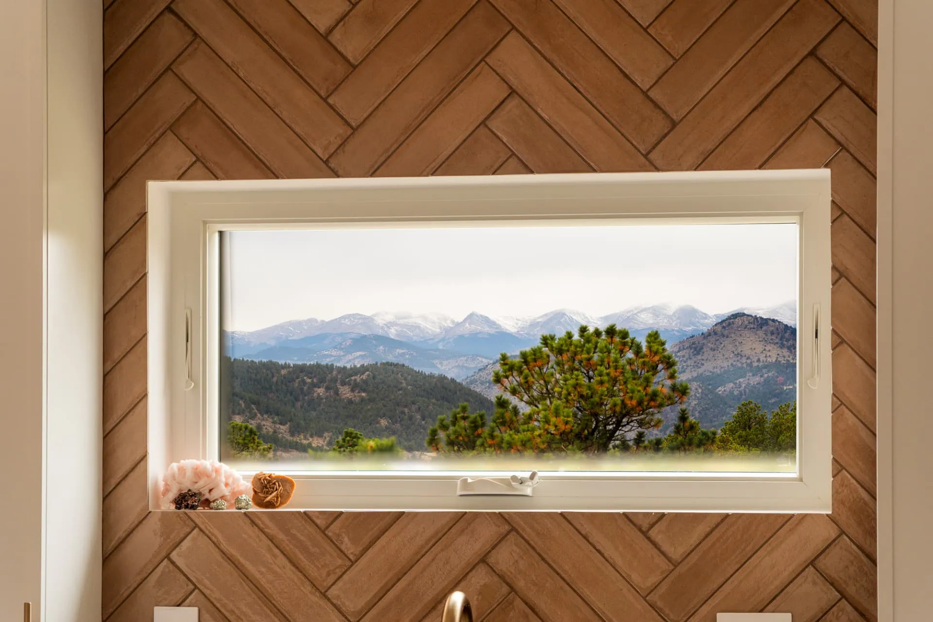 Picture window in a herringbone wood wall framing snow-capped peaks